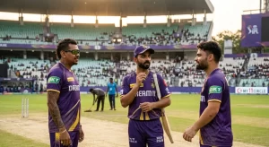 Three Kolkata Knight Riders players in purple and gold IPL 2026 jerseys — Sunil Narine (left, wearing sunglasses), Ajinkya Rahane (centre, holding a bat), and Rinku Singh (right) — engage in a pre-match discussion on the outfield at Eden Gardens, with groundstaff preparing the pitch and the partially filled stadium visible in the background.