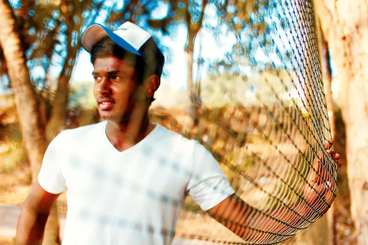 Young Sanju Samson standing beside a cricket practice net during his early playing years.