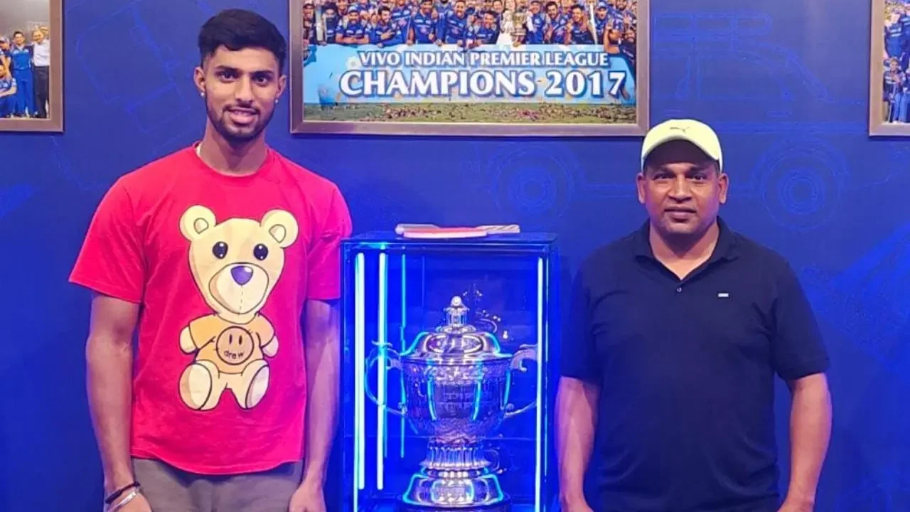 Tilak Varma standing with coach Salam Bayash beside an IPL trophy display at the Mumbai Indians facility.