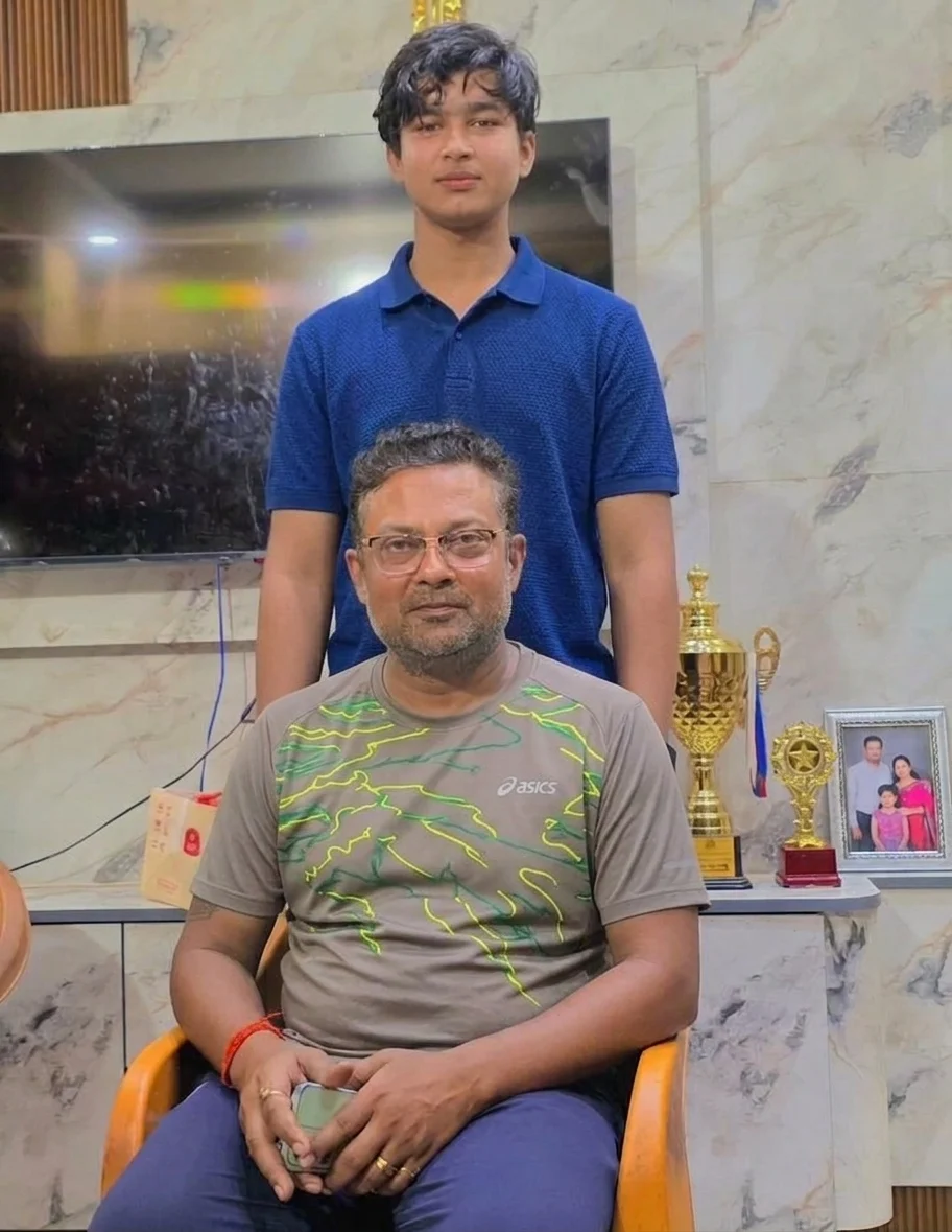 Vaibhav Sooryavanshi stands with his cricket coach Manish Ojha beside trophies and awards.