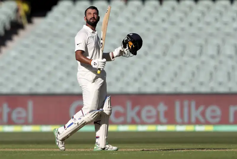 Indian Test batter in white cricket kit holding his bat and helmet after an innings, reflecting the patience and resilience highlighted in Cheteshwar Pujara’s biography.