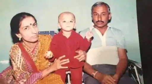Vintage childhood family photograph accompanying Cheteshwar Pujara’s early life, showing a young child seated between his mother and father.