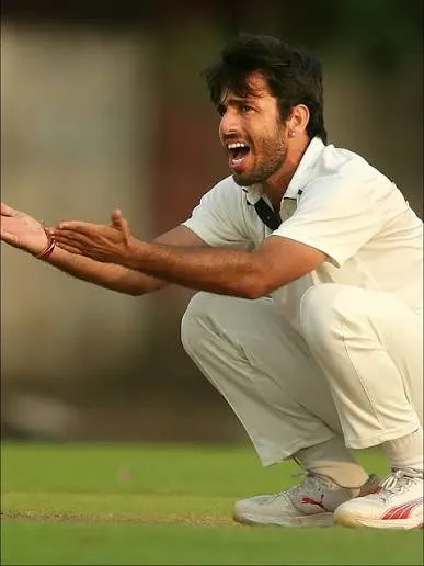 Young leg-spin bowler in white cricket kit crouches on the field and appeals during an early-career domestic match.