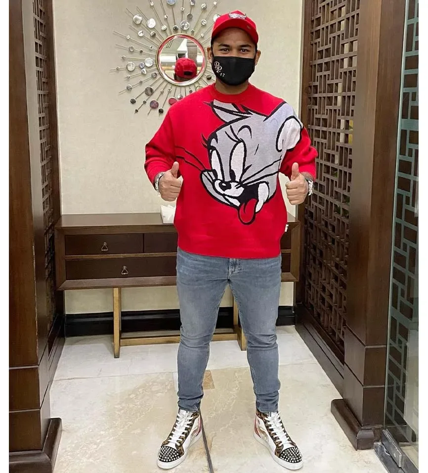 Rishabh Pant posing inside a modern residence wearing a red sweatshirt, cap and face mask.