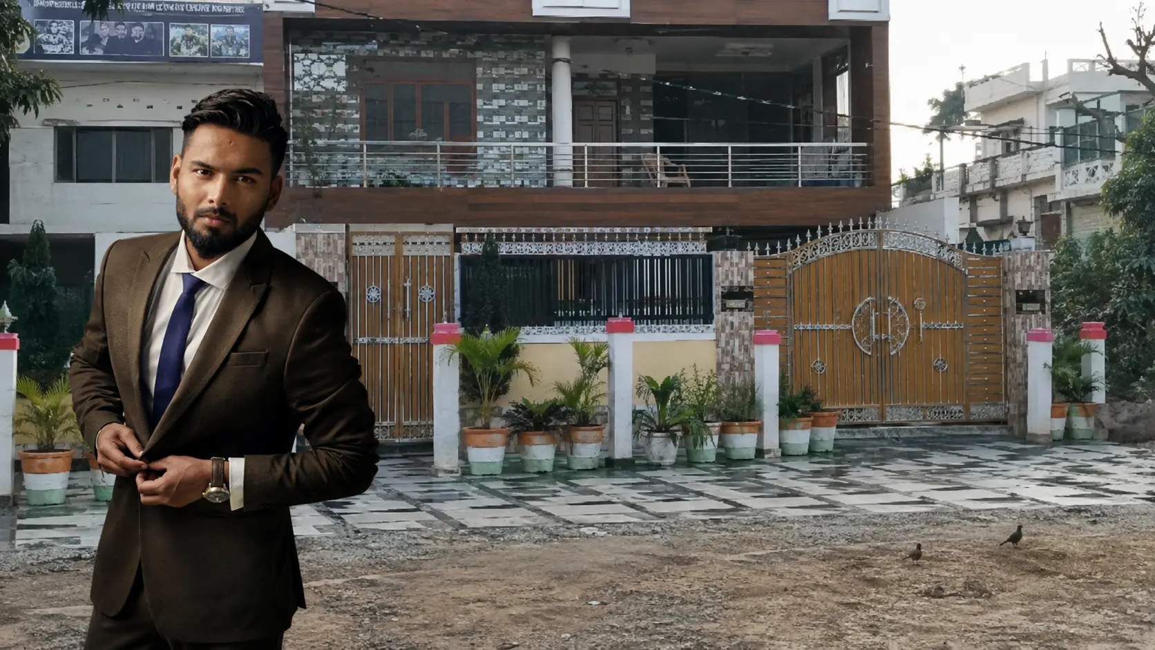 Rishabh Pant standing in formal attire outside his family house in Roorkee, Uttarakhand.