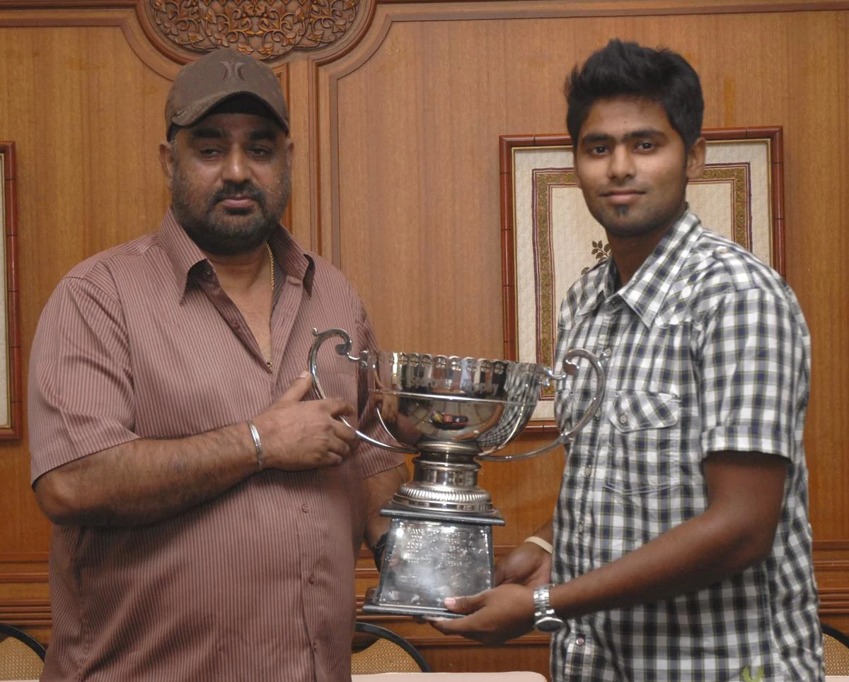 Young Suryakumar Yadav posing with an early cricket coach while holding a trophy.