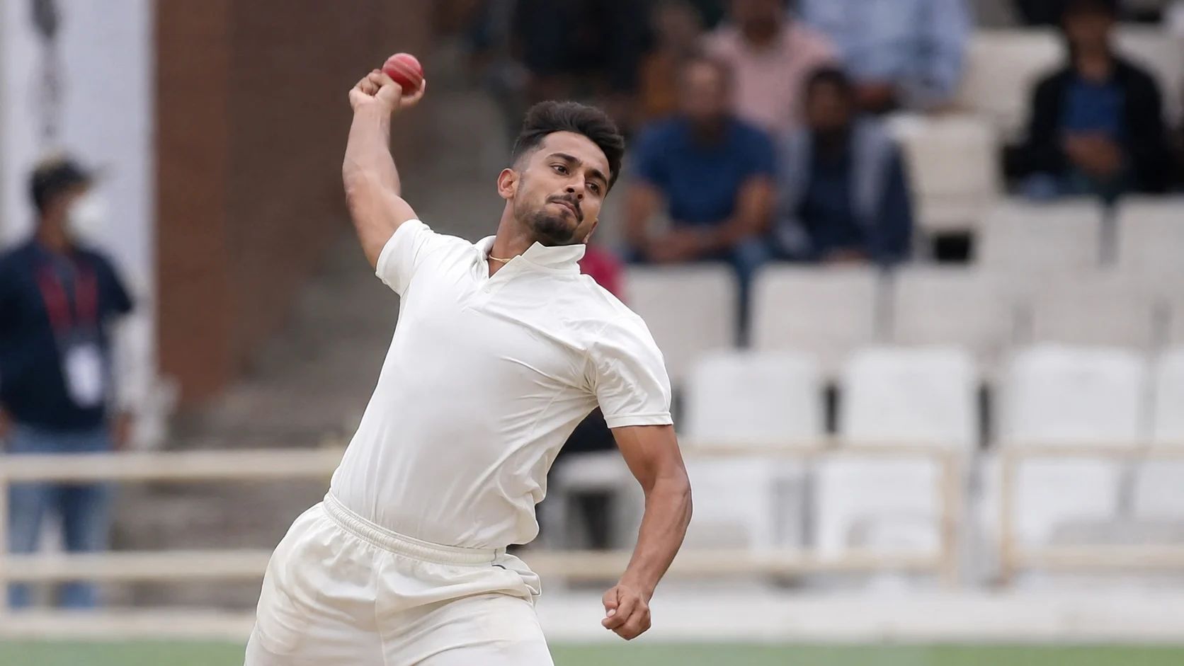 Umran Malik delivering a red ball in white cricket clothing during a domestic match.