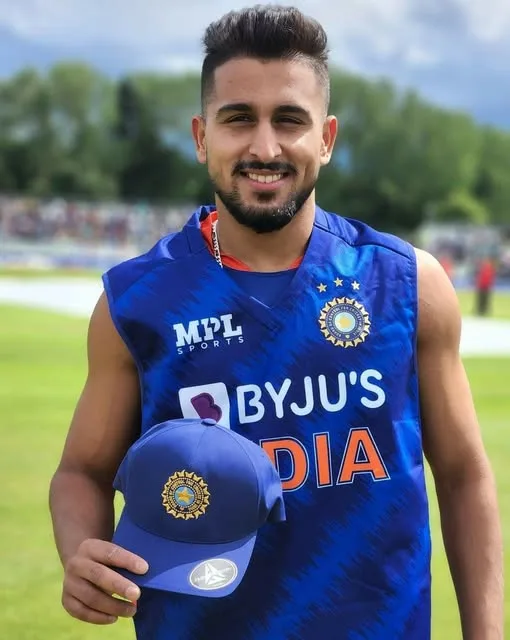 Umran Malik wearing India’s blue cricket training jersey and holding a national team cap on the field.