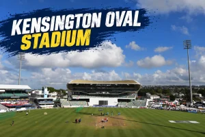 Wide view of Kensington Oval Stadium in Bridgetown, Barbados, showing the cricket pitch, outfield, stands, floodlights, and blue sky, with “Kensington Oval Stadium” displayed across the top.
