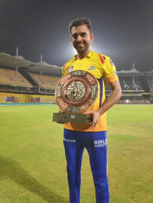 Deepak Chahar in Chennai Super Kings jersey holding a trophy on the cricket field during his successful IPL career.