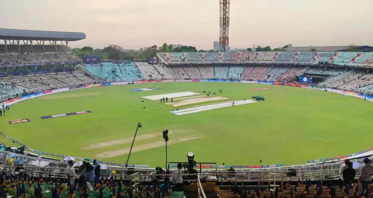 Eden Gardens cricket stadium in Kolkata showing the iconic ground with prepared pitch, floodlight tower, stadium seating sections with green and brown chairs, ground staff preparing covers, and spectators gathering before match - illustrating the historic venue's capacity of 63,000 and balanced black-soil pitch conditions for IPL, T20 World Cup, and international cricket matches