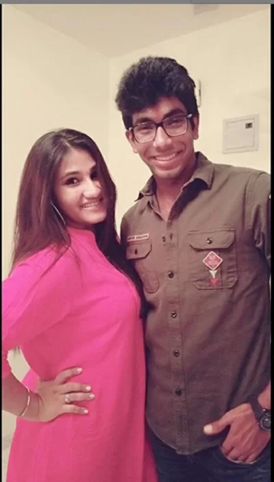 Young Indian cricketer wearing glasses and a brown shirt posing indoors with a female family member dressed in pink.
