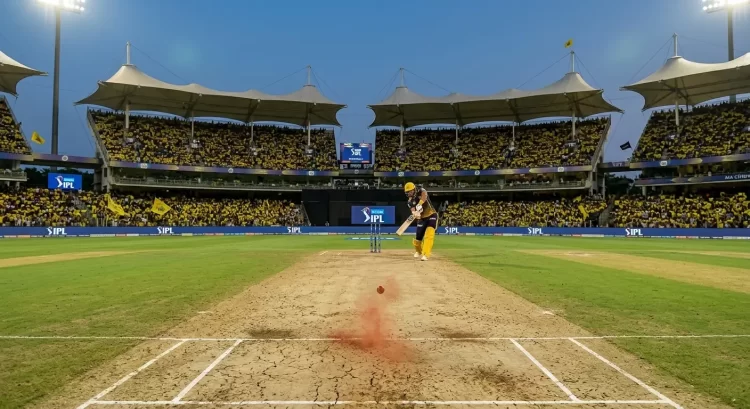 A batter in yellow CSK kit plays a shot on the dry, cracked, spin-friendly Chepauk pitch at MA Chidambaram Stadium during an IPL match, with a packed 50,000-strong Yellow Army crowd waving CSK flags under floodlights in the background.