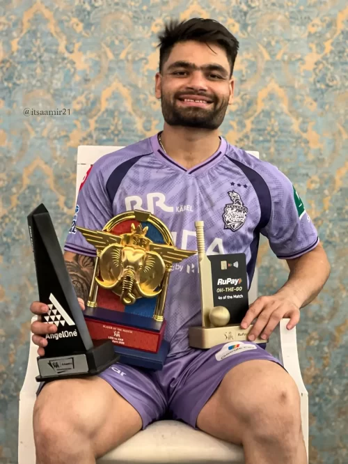Rinku Singh smiling in a Kolkata Knight Riders jersey while holding Player of the Match and other IPL awards