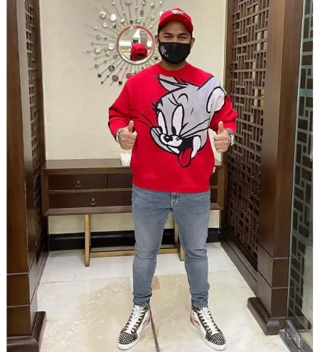 Rishabh Pant posing inside a modern residence wearing a red sweatshirt, cap and face mask.